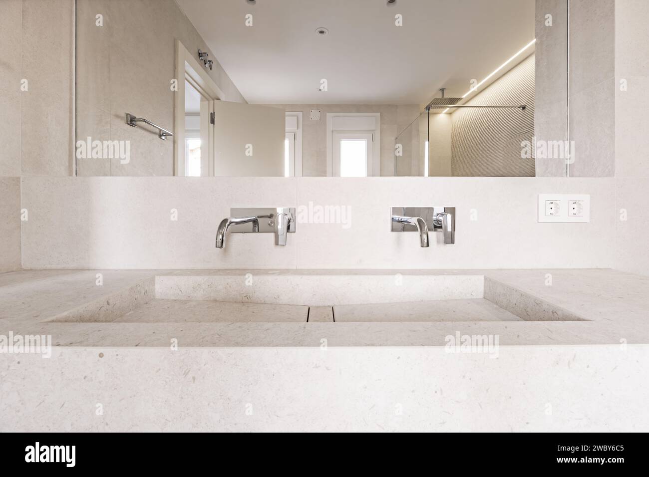 Immagine frontale di un bagno di nuova costruzione con armadietto con rubinetti in acciaio cromato, uno specchio integrato nella parete, un lavandino in pietra color crema e Foto Stock
