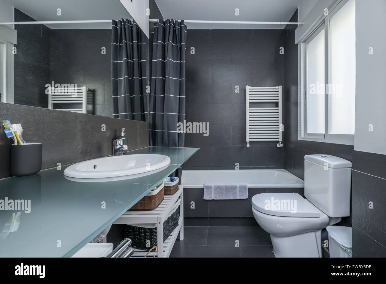 un bagno dal design moderno con pareti in porcellana grigio opaco, specchi integrati nella parete e ripiano in vetro temperato Foto Stock