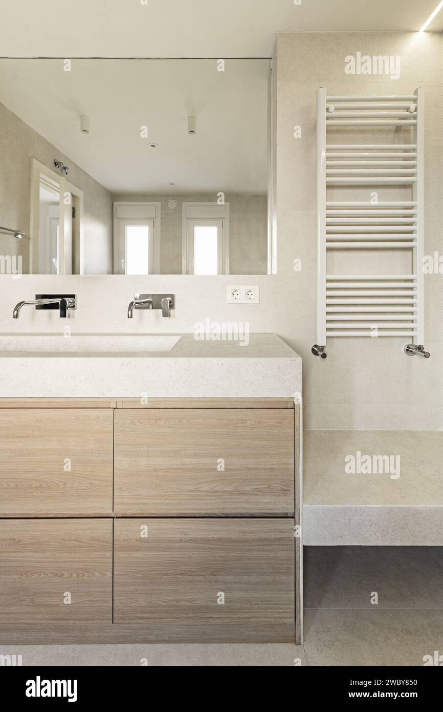 Bagno con mobili in quercia, specchio senza telaio, rubinetti di design e radiatore per asciugamani bianchi Foto Stock
