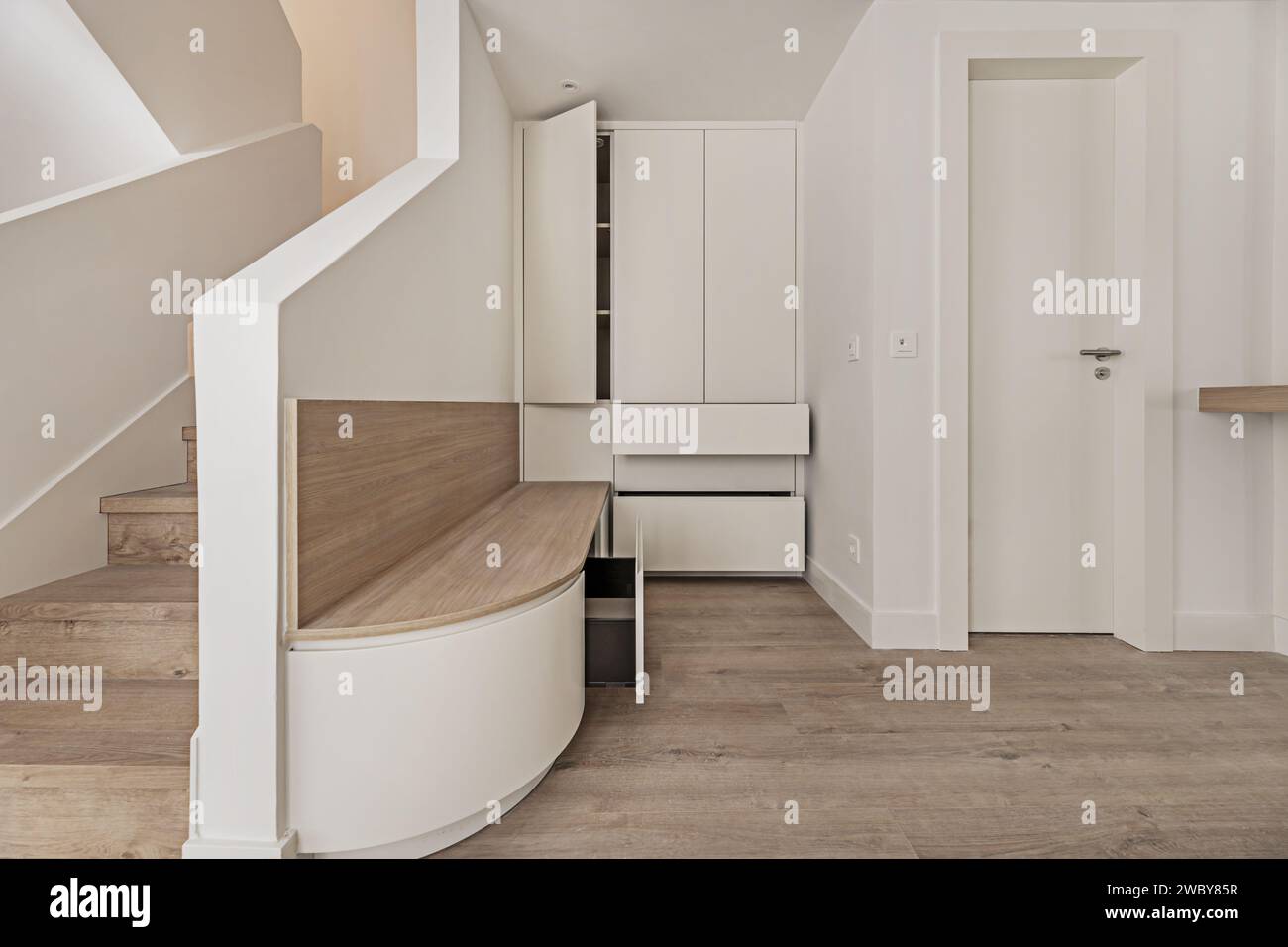 Corridoio di una casa moderna recentemente rinnovata con una panca in legno di quercia bianca con cassetti e un mobile bianco vicino alle scale per salire Foto Stock