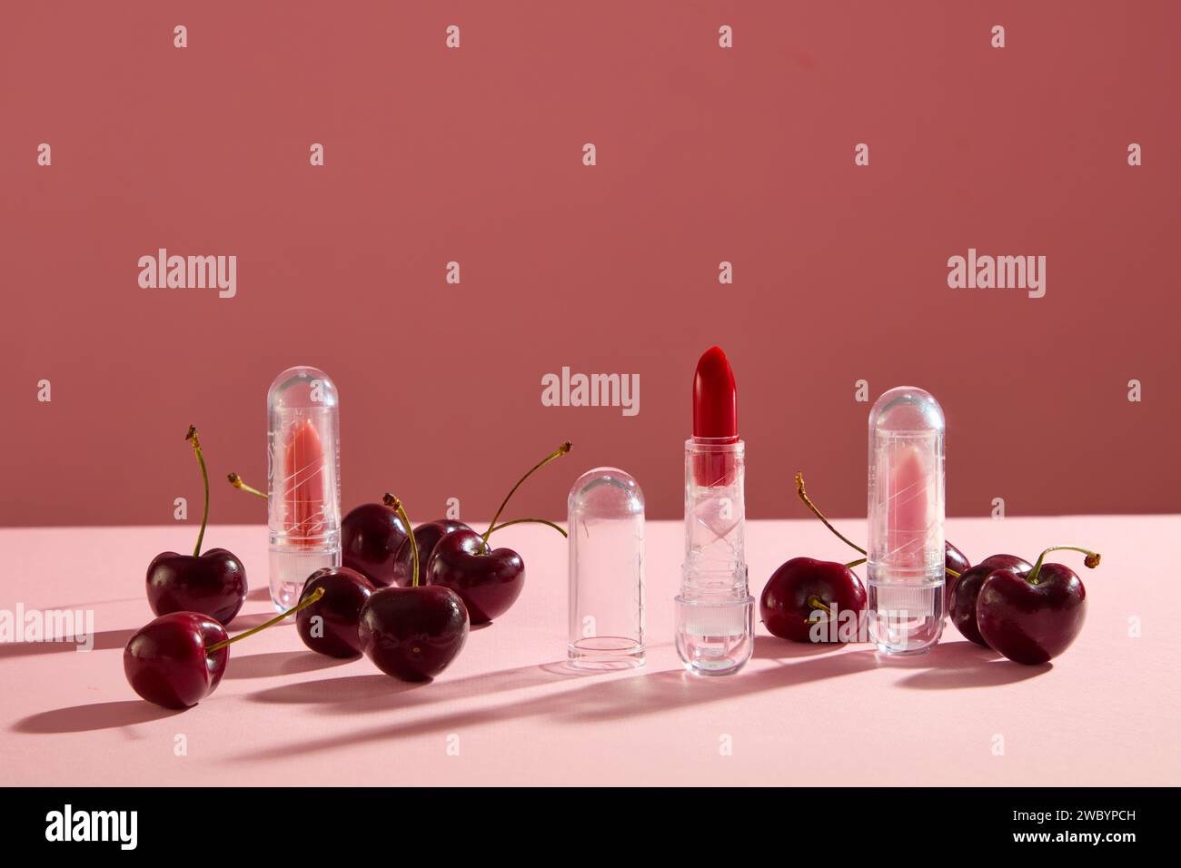 Tre rossetti in colori diversi decorati con ciliegie su sfondo rosa. Le ciliegie hanno un ricco contenuto di antiossidanti Foto Stock