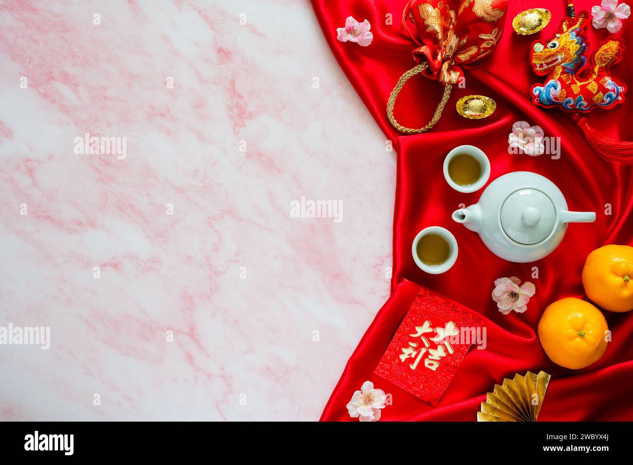 Set da tè su sfondo di tessuto rosso con buste rosse o ang bao (parola significa auspice), sacchetto rosso, lingotti (parola significa ricchezza), drago pendente sospeso e. Foto Stock