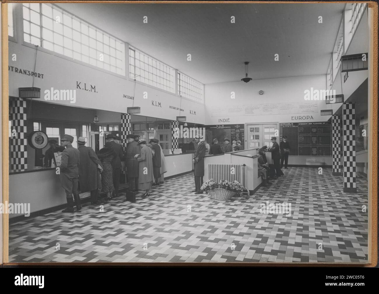 Interno dell'edificio della stazione del comune di Schiphol Airport, 1928 - 1940 Fotografia album rivista con una foto di banchi di varie compagnie aeree, cartelli di partenza, passeggeri e personale di terra nell'edificio della stazione del comune di Schiphol Airport. Parte dell'album commemorativo della linea Indies di KLM, parte II Carta Schiphol. supporto fotografico. cartone gelatina stampa argento traffico aereo, aviazione. viaggi; turismo. aeroporto, aeroporto. Arrivo e ritorno  Schiphol in viaggio Foto Stock