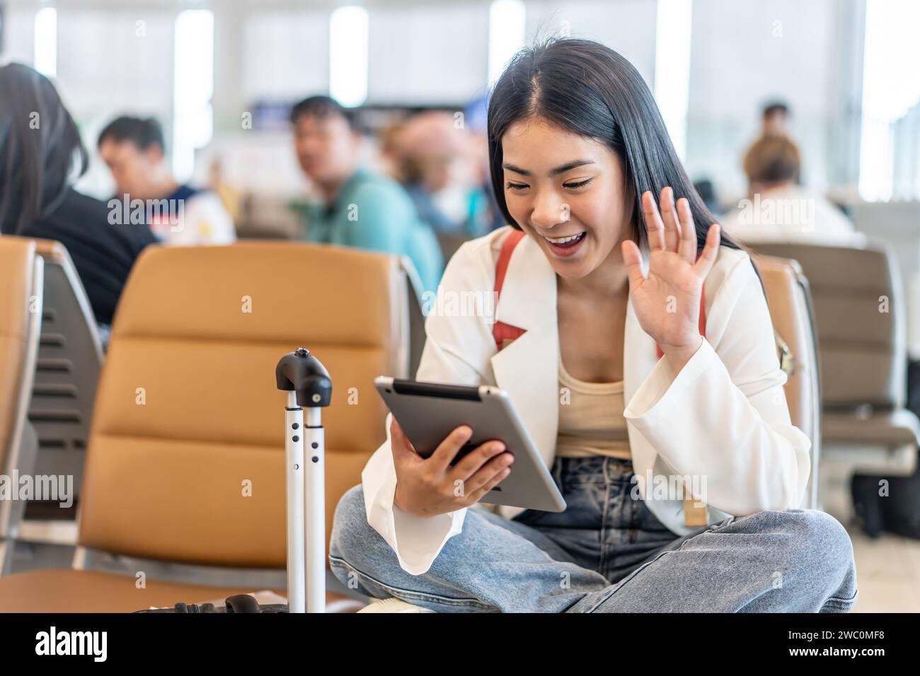 Una giovane donna asiatica in una videochiamata sul suo tablet al terminal dell'aeroporto Foto Stock