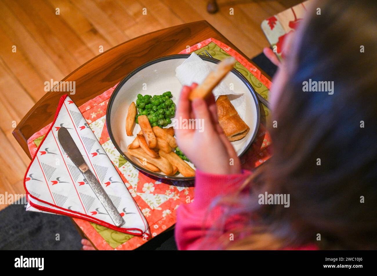 Bambina di 7 anni che mangia salsiccia, patatine fritte e piselli Foto Stock