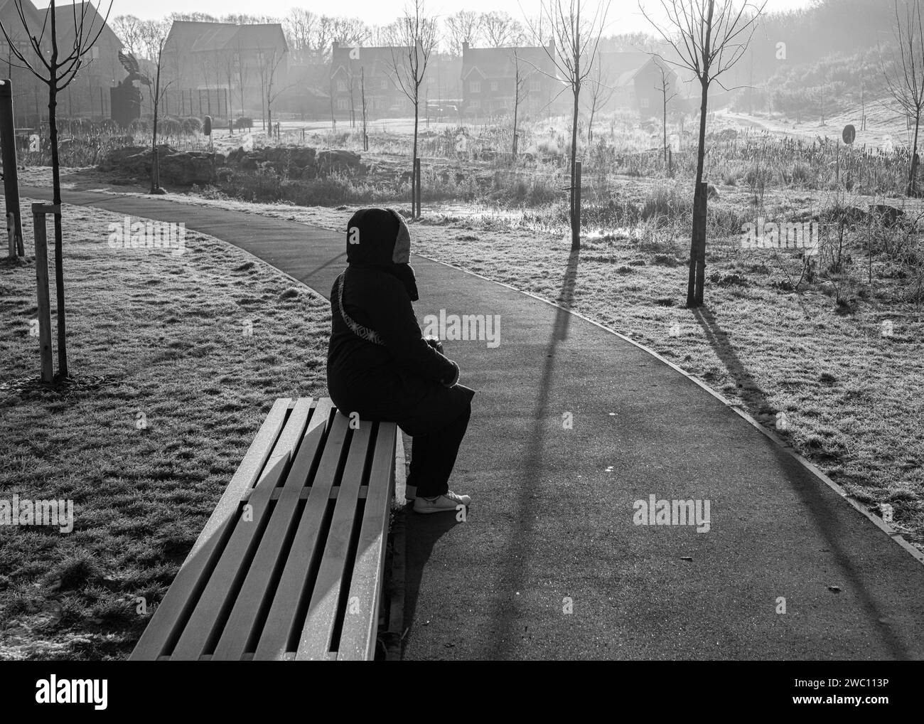 Un'immagine in bianco e nero di una donna seduta su una panchina del parco in una mattinata gelata a Kings Weald, Burgess Hill, che guarda l'alba di gennaio Foto Stock