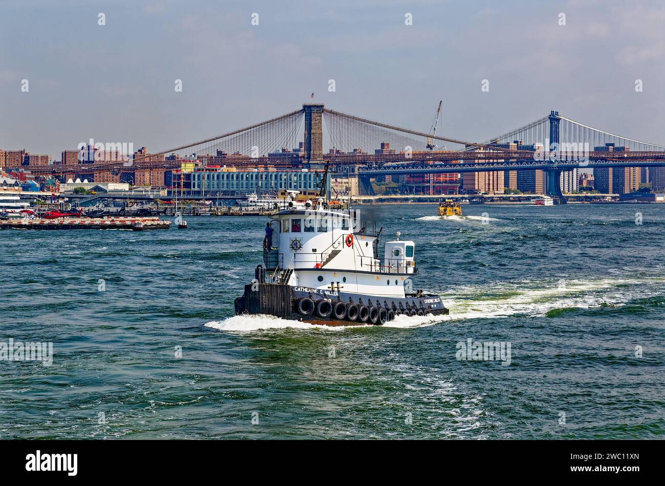 Il rimorchiatore Catherine C. Miller e le acque non identificate dell'East River dove incontra New York Bay; Brooklyn e Manhattan Bridges sullo sfondo. Foto Stock