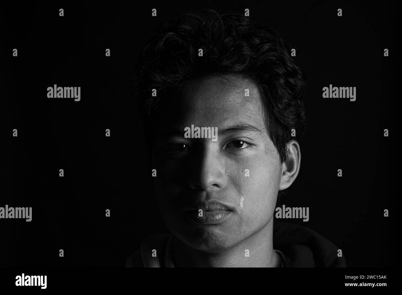 Un ritratto ravvicinato di un uomo con lacrime sul viso su sfondo scuro in scala di grigi Foto Stock