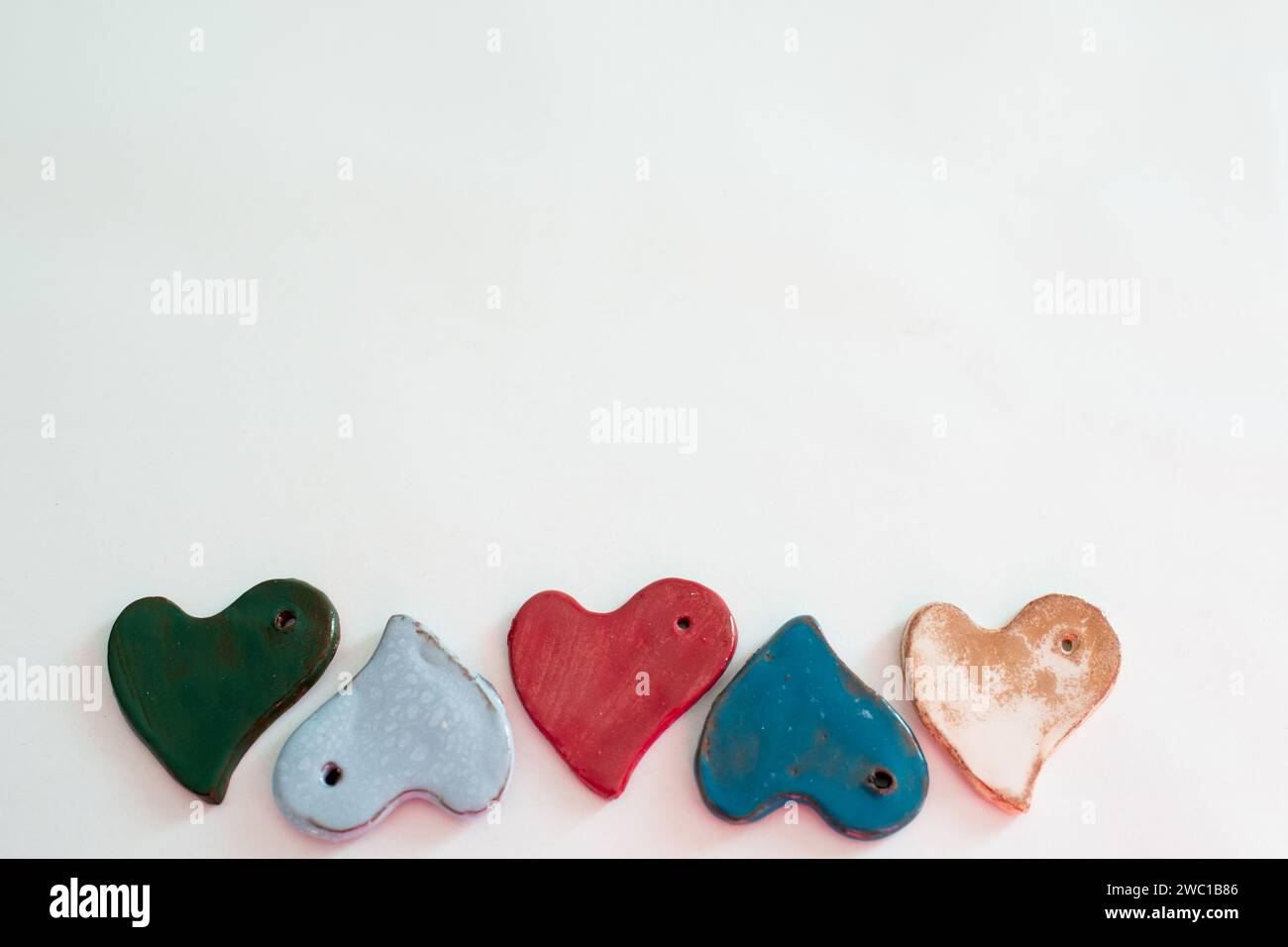 Diversità e amore. Piccoli pezzi in ceramica a forma di cuore. Sfondo bianco Foto Stock