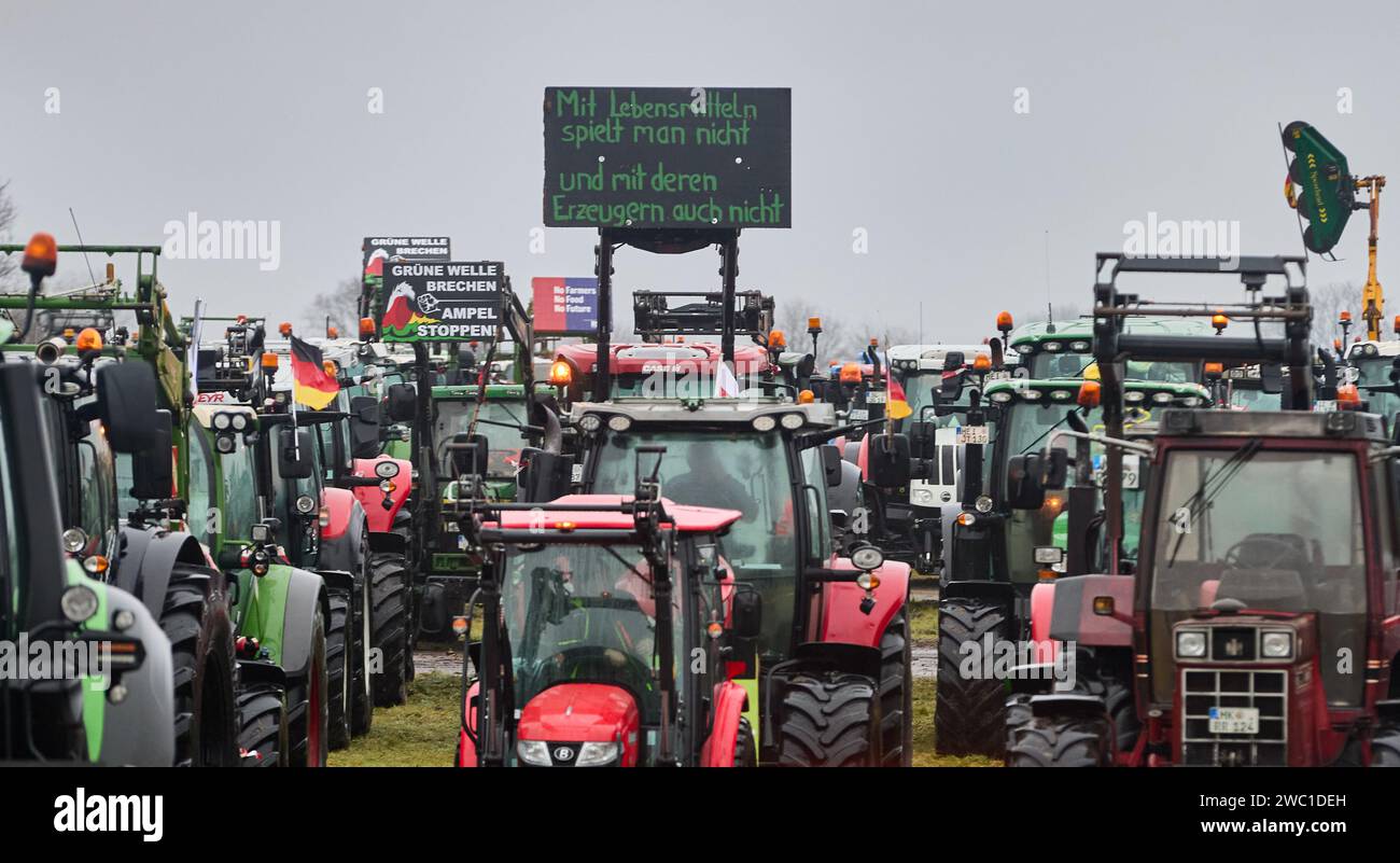 Hohenlockstedt, Germania. 13 gennaio 2024. Un trattore con uno striscione che recita "non giochi con il cibo e non giochi nemmeno con i produttori" si trova accanto a molti altri trattori presso l'Hungry Wolf Airfield. La Schleswig-Holstein Construction Industry Association ha chiesto una grande dimostrazione da parte delle imprese edili. Crediti: Georg Wendt/dpa/Alamy Live News Foto Stock