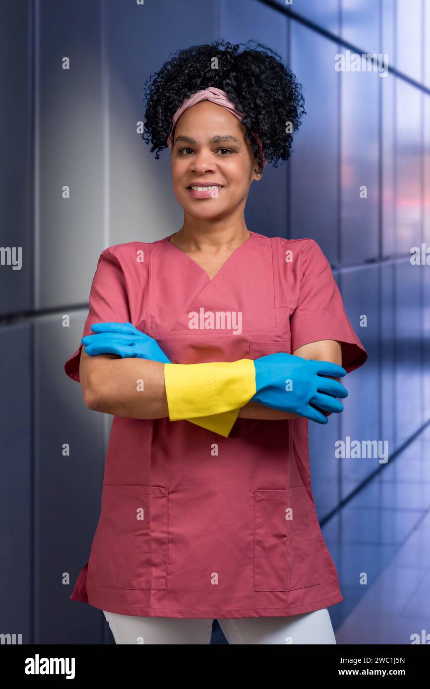 Simpatico pulitore femminile dell'America Latina con abiti da lavoro e guanti in gomma con braccia piegate Foto Stock