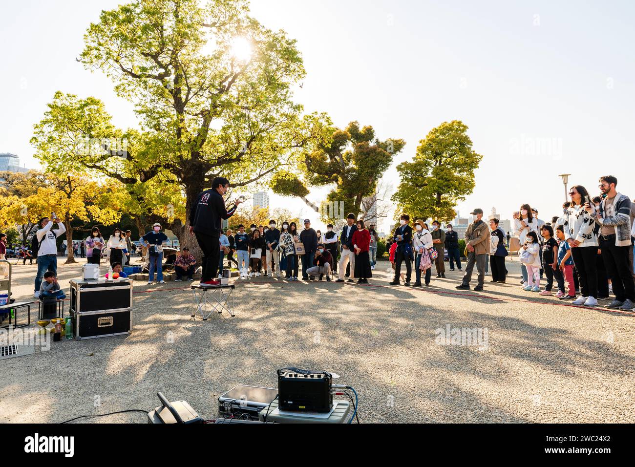 Giocoliere in piedi su un piccolo tavolo per intrattenere una piccola folla di persone che guardano il sole luminoso in una giornata primaverile al Parco del Castello di Osaka. Foto Stock