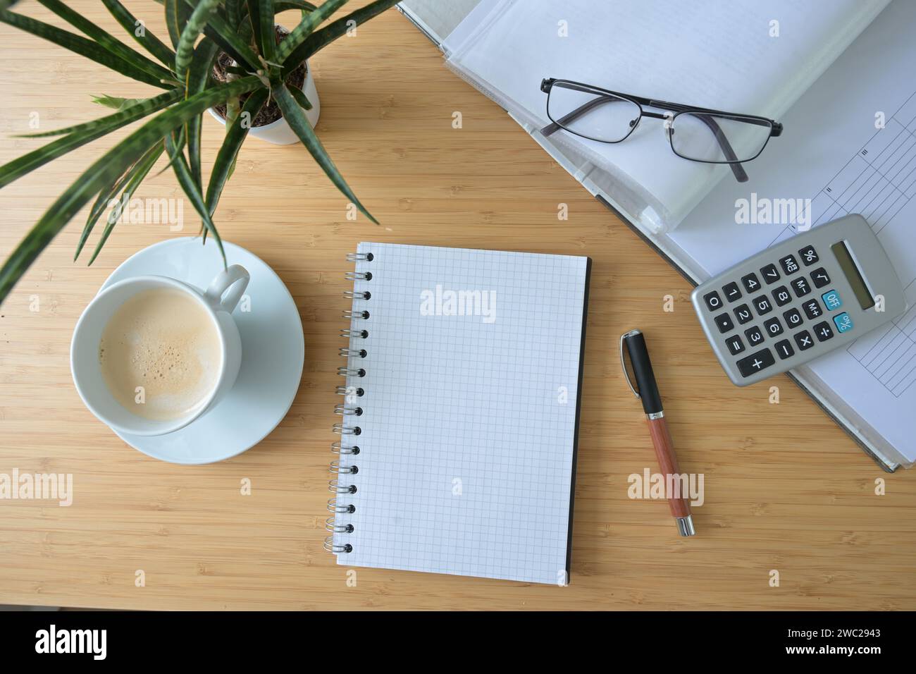 Modello di blocco note a spirale vuota su una scrivania con cartella, calcolatrice, tazza da caffè e impianto, concetto per contabilità aziendale e finanziaria, angolo alto Foto Stock