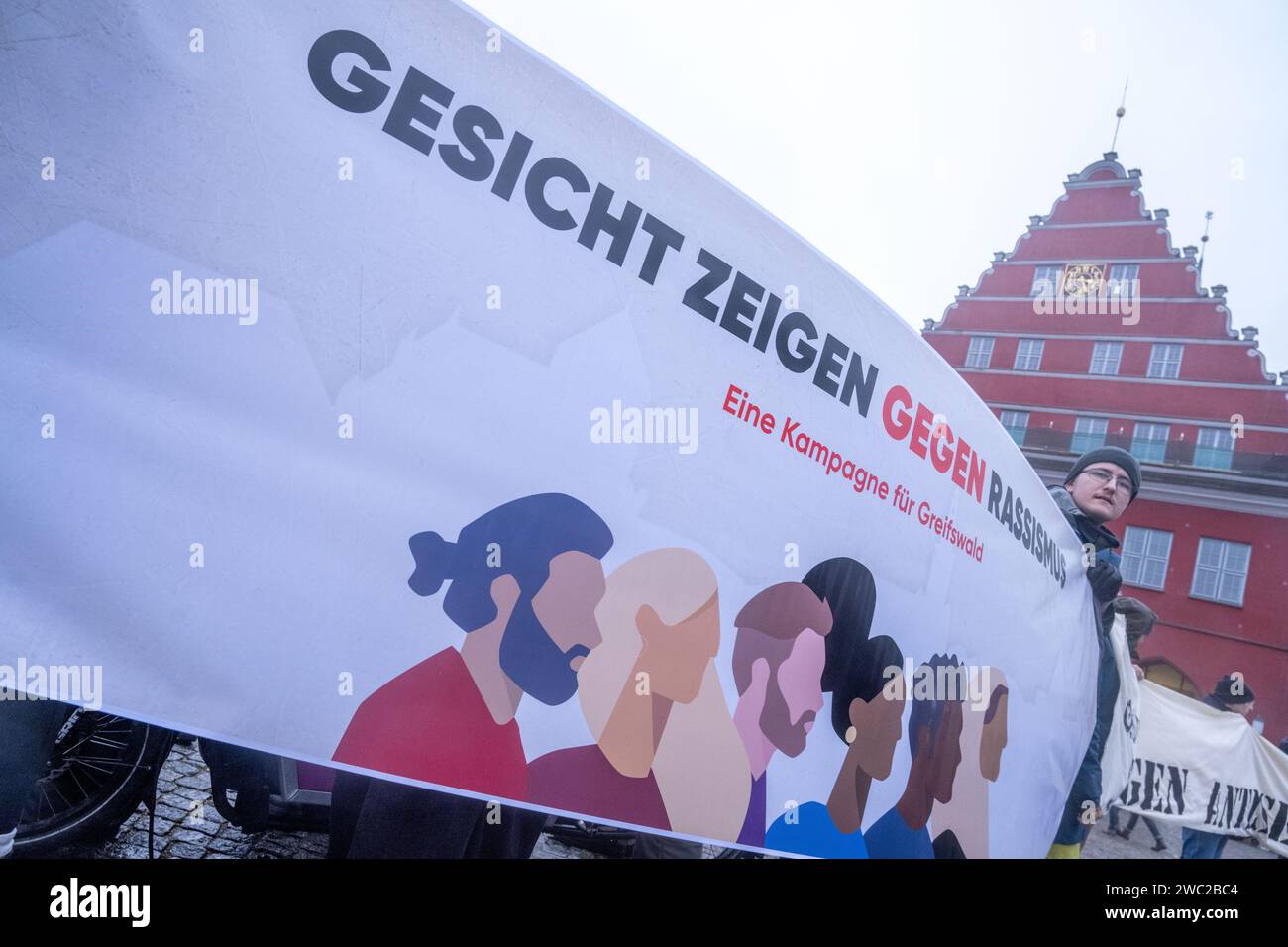 Greifswald, Germania. 13 gennaio 2024. Secondo la polizia, 1.200 persone hanno manifestato contro il razzismo nella piazza del mercato di Greifswald di fronte al municipio alla luce dei recenti attacchi nella città. Con il motto "Mostra la tua faccia - contro il razzismo”, i residenti di Greifswald hanno parlato in una manifestazione di sabato pomeriggio delle loro esperienze nella vita quotidiana, del loro lavoro, dei loro studi e del loro impegno sociale. Crediti: Stefan Sauer/dpa/Alamy Live News Foto Stock