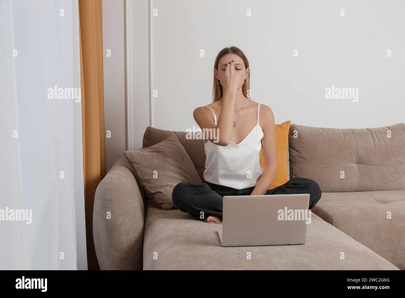 Donna che pratica meditazione ed esercizi di respirazione sul divano nel soggiorno, rilassata, accogliente e consapevole Foto Stock