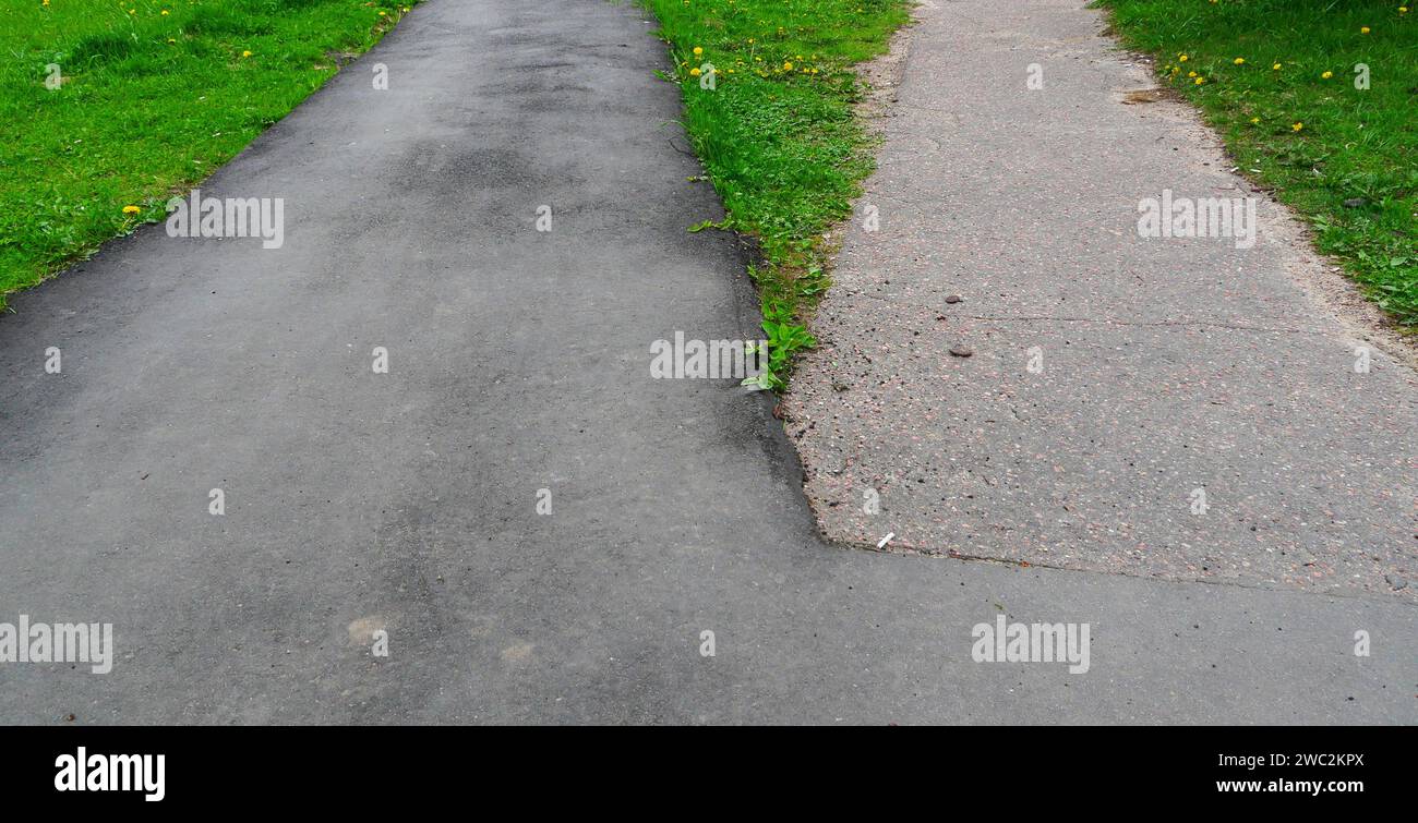 Due piccole strade asfaltate in erba verde. Due marciapiedi di asfalto adiacenti. Foto Stock