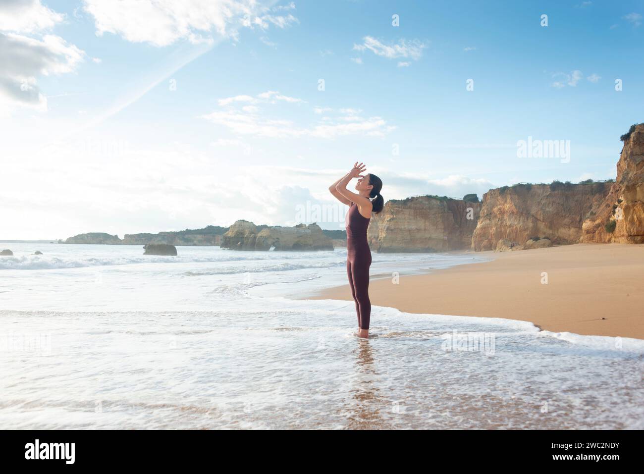 Vista laterale di una donna che fa yoga in spiaggia in piedi in mare mentre meditava Foto Stock