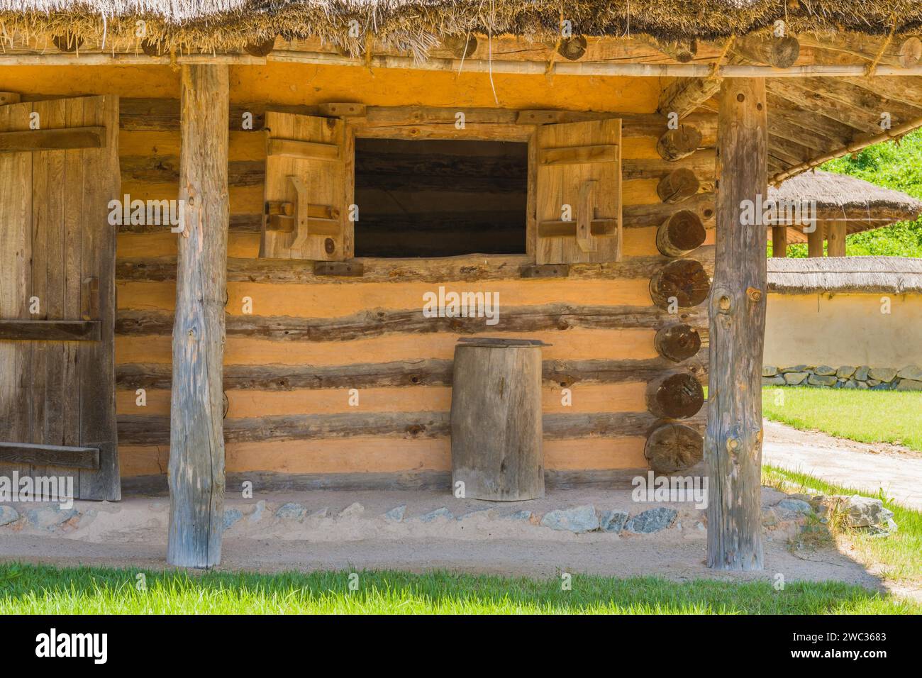 Esterno della cabina in legno con portico in cemento e pietra e tetto coperto in paglia Foto Stock