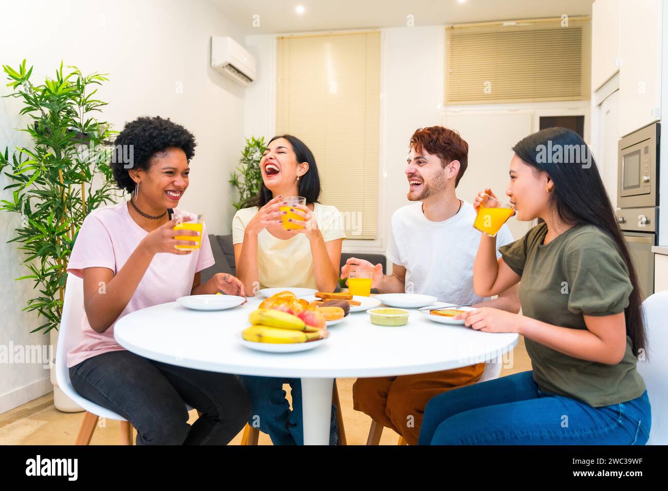 Giovane gruppo multietnico di amici che ridono mentre mangiano una sana colazione a casa Foto Stock