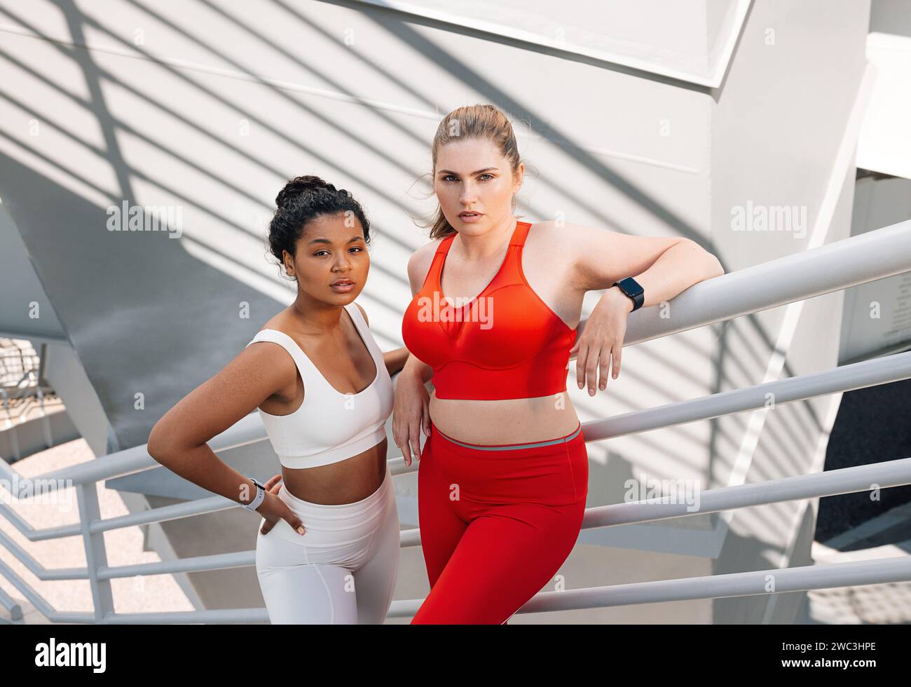 Ritratto di due donne più taglie in abiti sportivi in piedi insieme. Due donne in abbigliamento fitness in piedi sulle scale di un ponte e guardano la camer Foto Stock