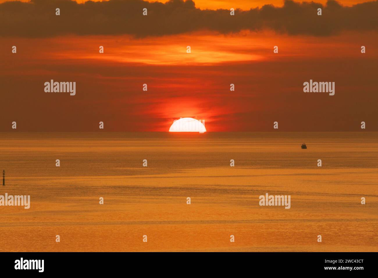 La barca siede in un mare calmo mentre il grande sole arancione tramonta sotto la linea dell'orizzonte. Foto Stock