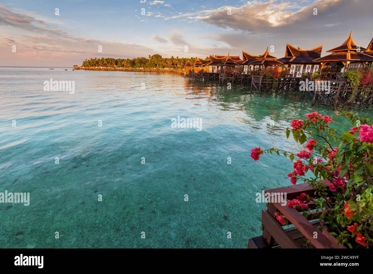 Capanne su palafitte si trovano sopra le limpide acque tropicali di un lussuoso hotel resort mentre il sole tramonta Foto Stock