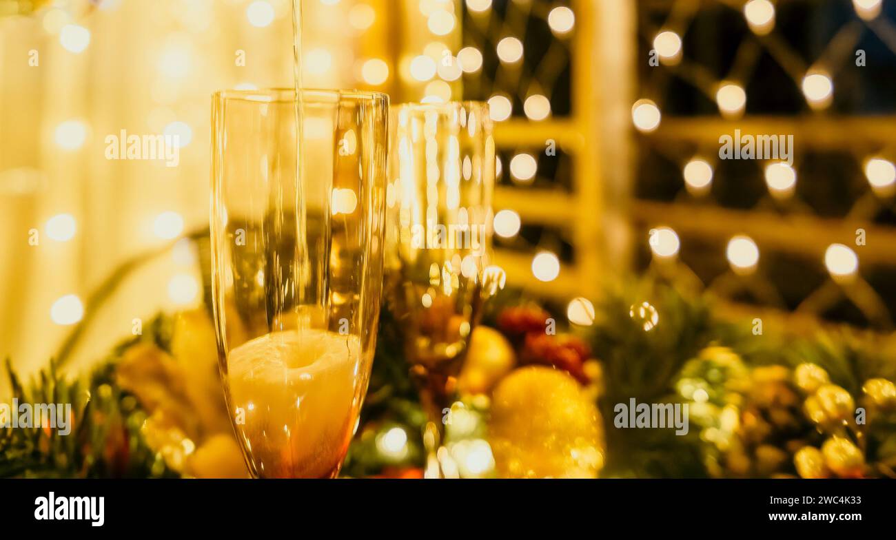 Due bicchieri di champagne ripieni di champagne sono collocati su un tavolo con disposizione a base di frutta. Gli occhiali sono circondati da luci che creano un'atmosfera festosa Foto Stock