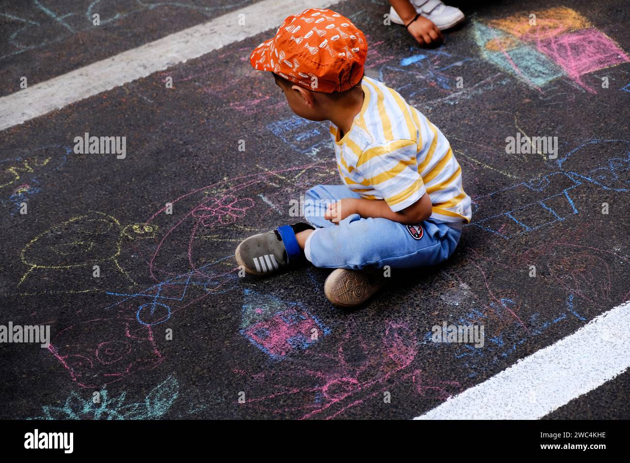 Bambino indiano che disegna con un gesso all'aperto. Immagini per bambini, creatività su strada grigia, attività all'aperto per bambini. vista dall'alto. Foto Stock