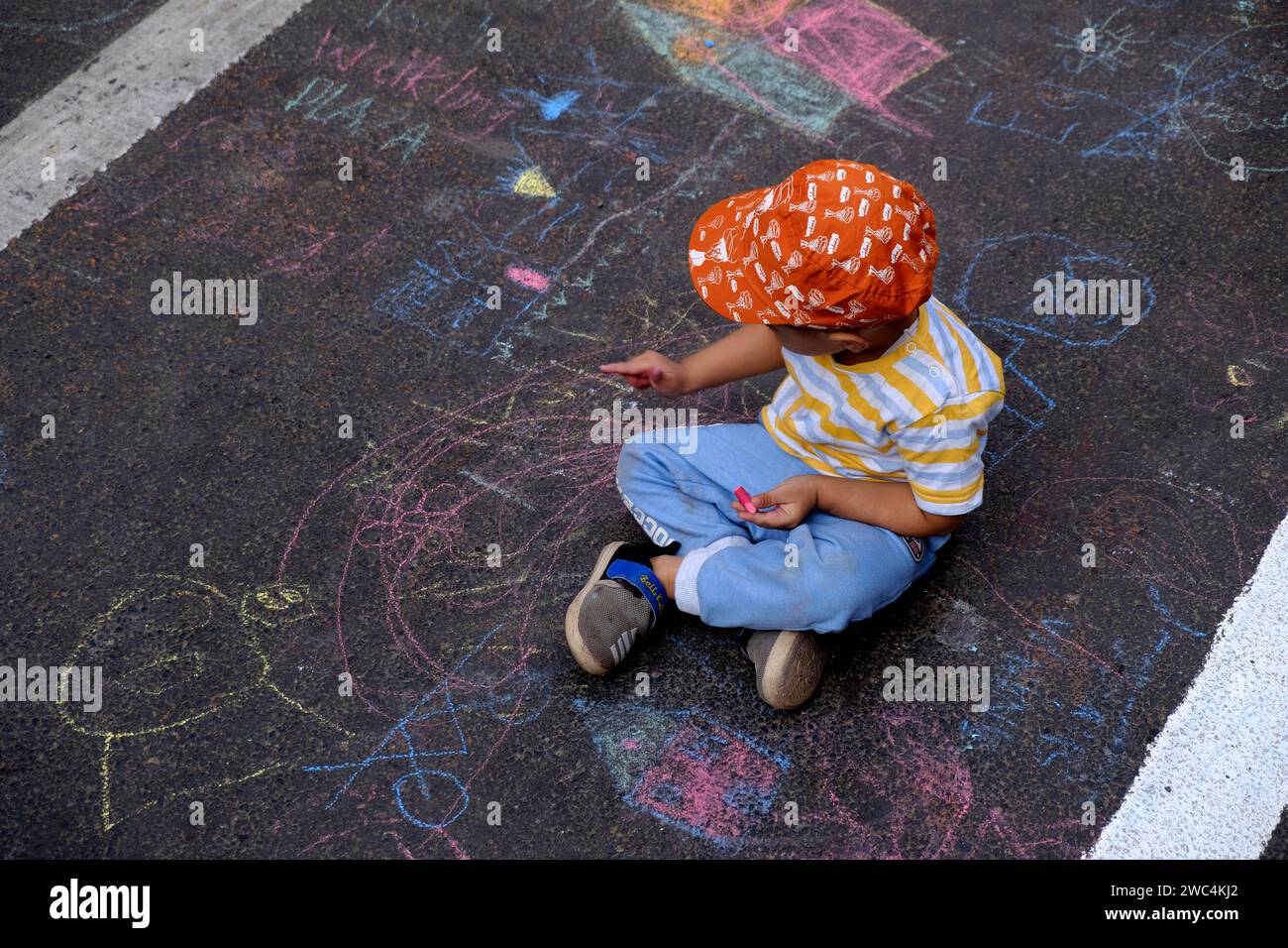 Bambino indiano che disegna con un gesso all'aperto. Immagini per bambini, creatività su strada grigia, attività all'aperto per bambini. vista dall'alto. Foto Stock