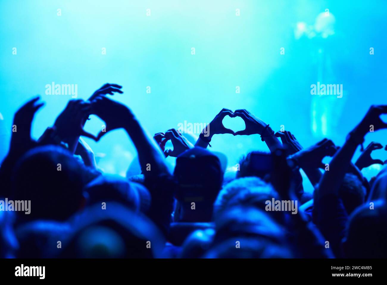 Persone, cuore mani e folla con luce blu per concerti musicali per amore, sostegno e cura dell'artista. Pubblico, fan e vita notturna insieme Foto Stock