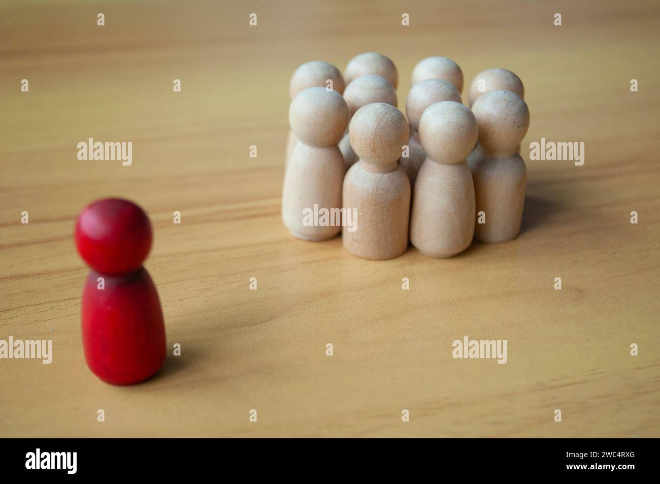 Bambola di legno rossa separata da altre bambole. Rappresentare la leadership o l'isolamento. Foto Stock