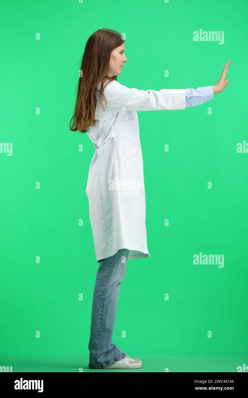 Una dottoressa donna, a tutta lunghezza, su sfondo verde, mostra un segnale di stop Foto Stock