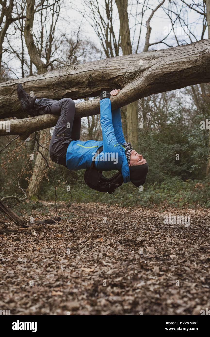 Una donna si scherza in giro appesa a testa in giù su un albero caduto nel bosco Foto Stock