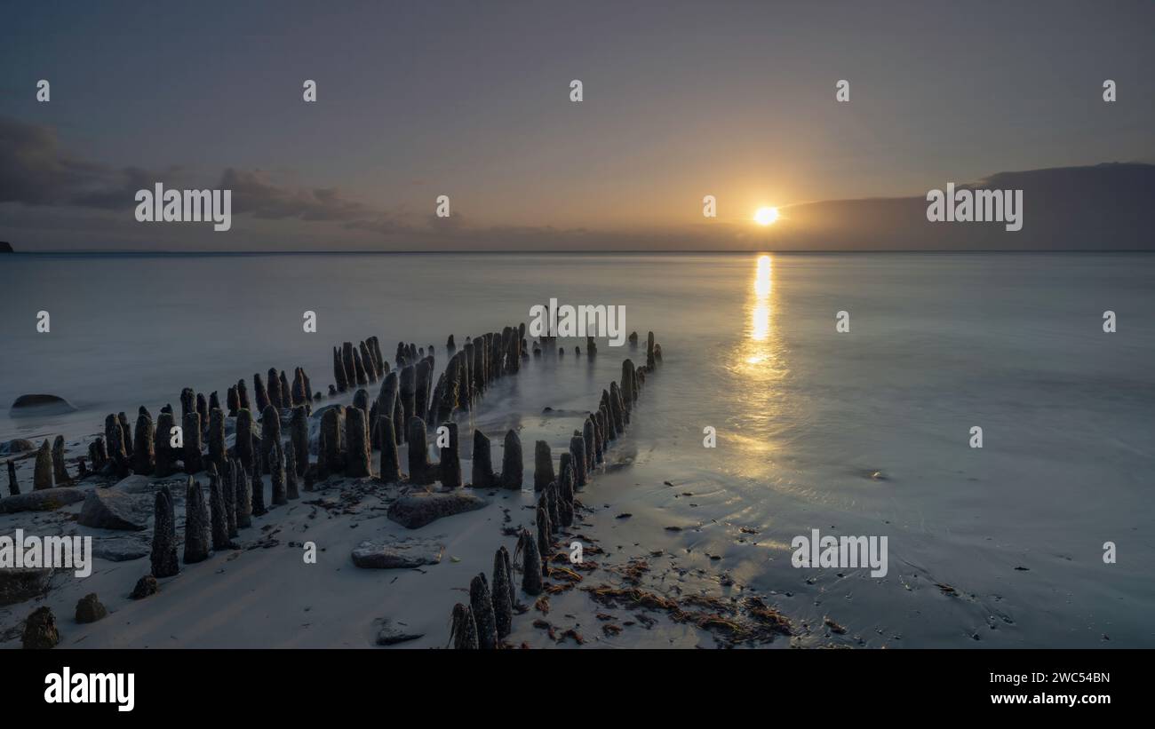 Una vista panoramica delle colonne di legno sulla spiaggia contro il mare al tramonto Foto Stock