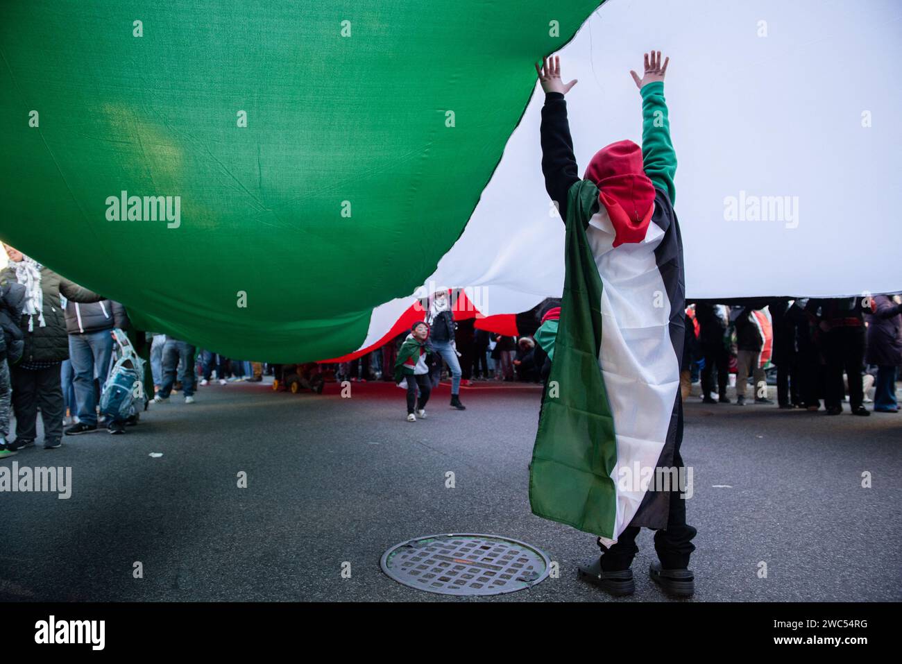 Washington, Stati Uniti. 13 gennaio 2024. I bambini giocano sotto una grande bandiera palestinese nella marcia su Washington per Gaza a Washington, DC, sabato 13 gennaio 2023. Migliaia di persone hanno partecipato alla marcia e alle proteste, molte delle quali hanno chiesto un cessate il fuoco e criticato il presidente Biden per aver sostenuto Israele. Foto di Annabelle Gordon/CNP/ABACAPRESS.COM Credit: Abaca Press/Alamy Live News Foto Stock