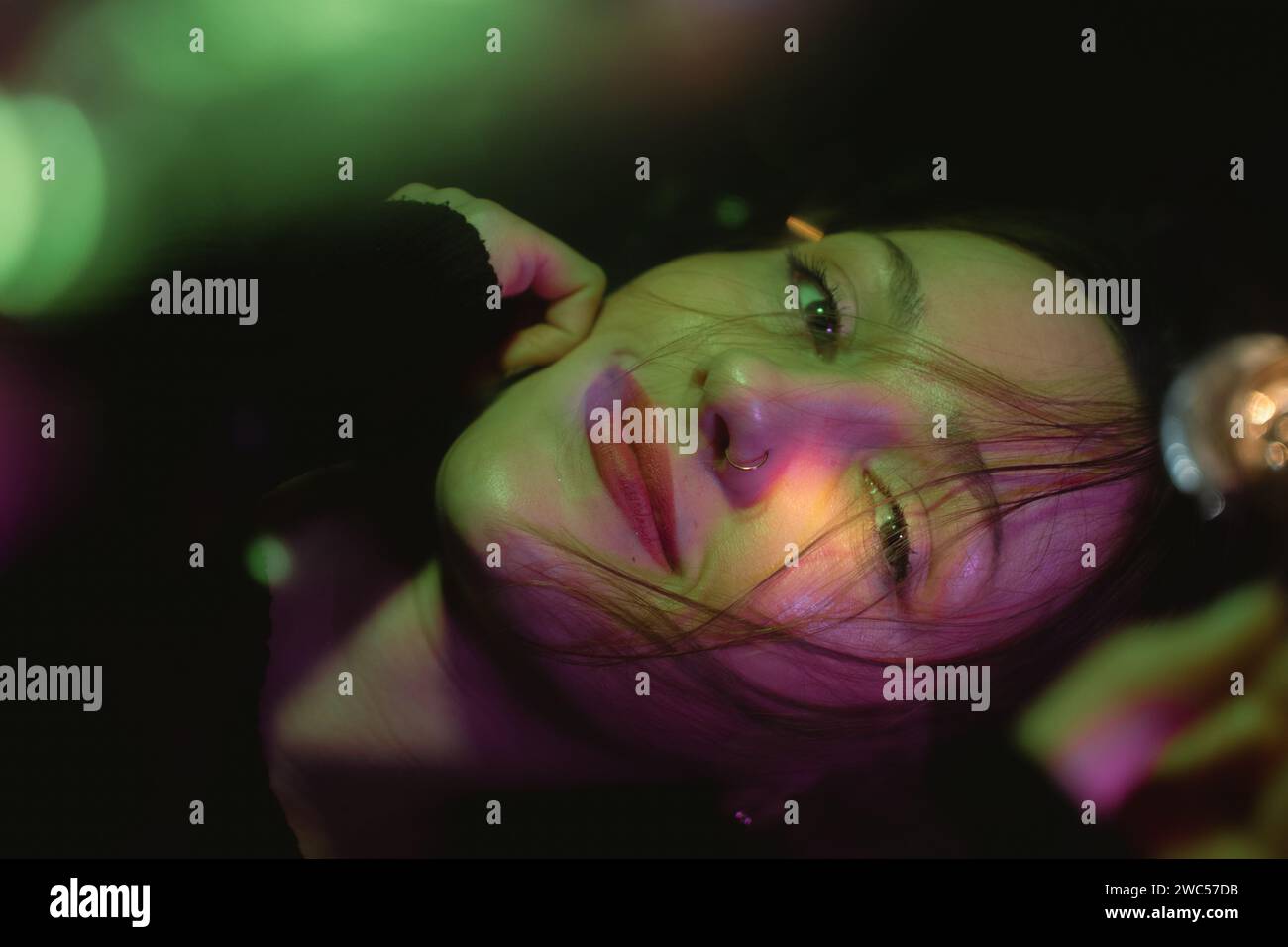 Una giovane donna attraente con un sorriso radioso tiene i suoi capelli lussureggianti in una posa drammatica su uno sfondo scuro Foto Stock
