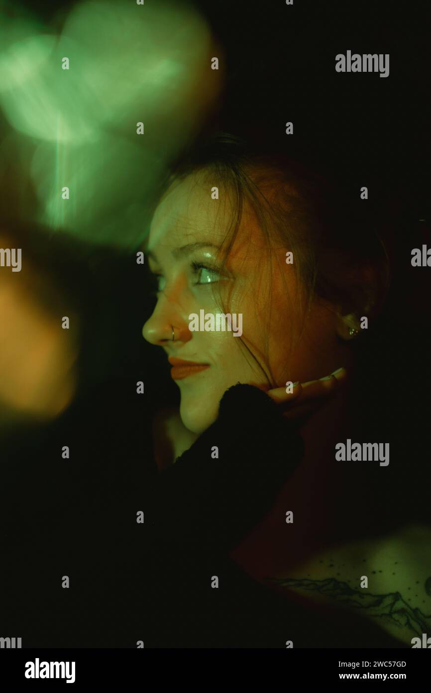 Una donna misteriosa con uno sfondo scuro guarda verso l'alto a destra, dando uno sguardo alle spalle Foto Stock
