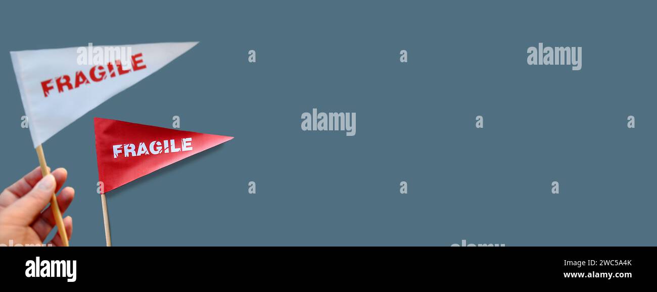 Piccoli flag di carta in mano con l'avvertenza "fragile" come etichetta. Il concetto di prodotti fragili. Sfondo monocromatico. Copia spazio Foto Stock