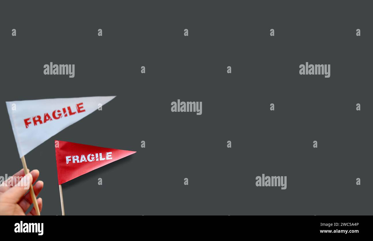 Piccoli flag di carta in mano con l'avvertenza "fragile" come etichetta. Il concetto di prodotti fragili. Sfondo monocromatico. Copia spazio Foto Stock