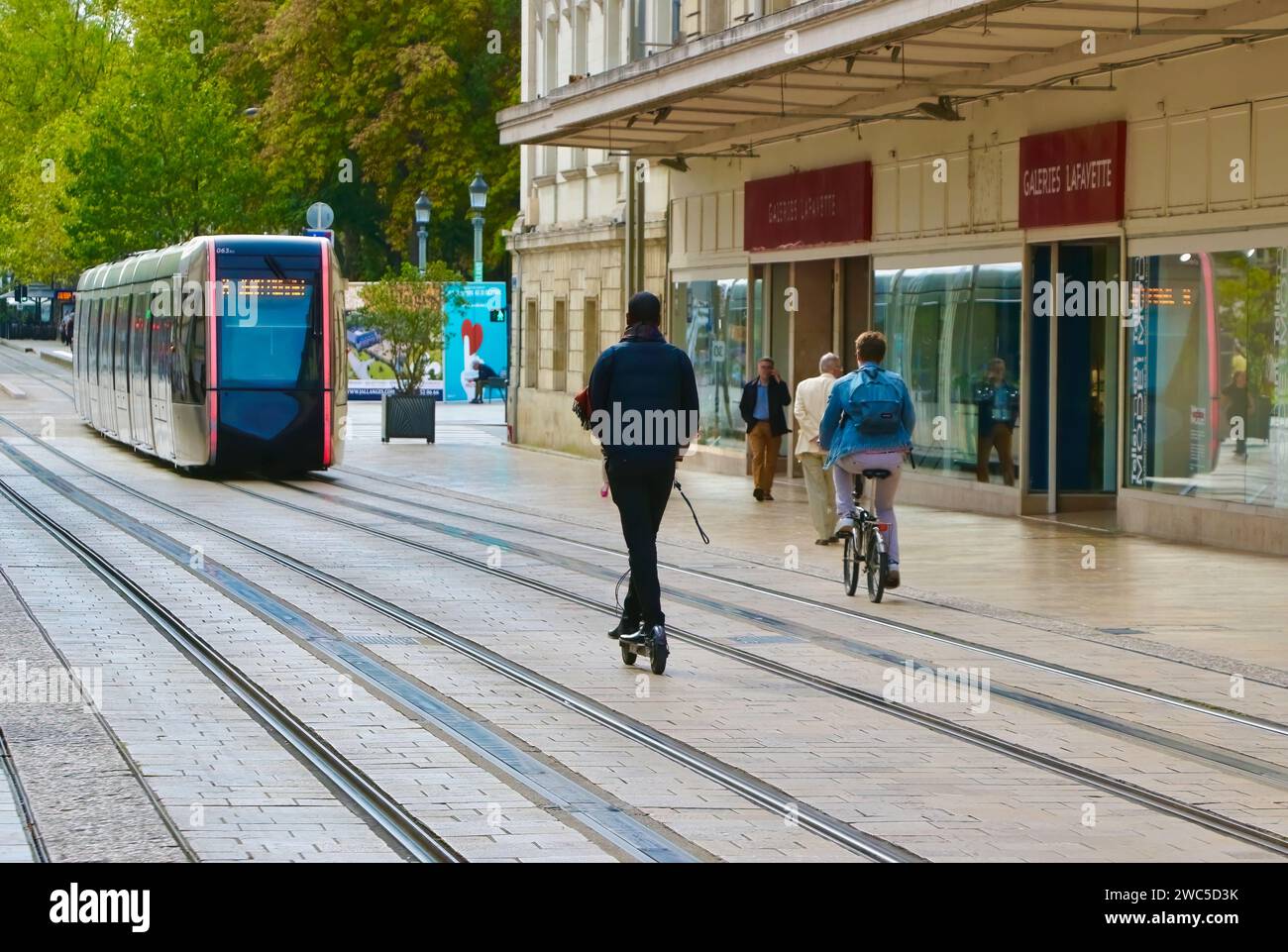 Un treno Citadis 402 di Tours tram, bicicletta e scooter elettrico passando davanti al grande magazzino Galeries Lafayette Rue Nationale Tours France Foto Stock