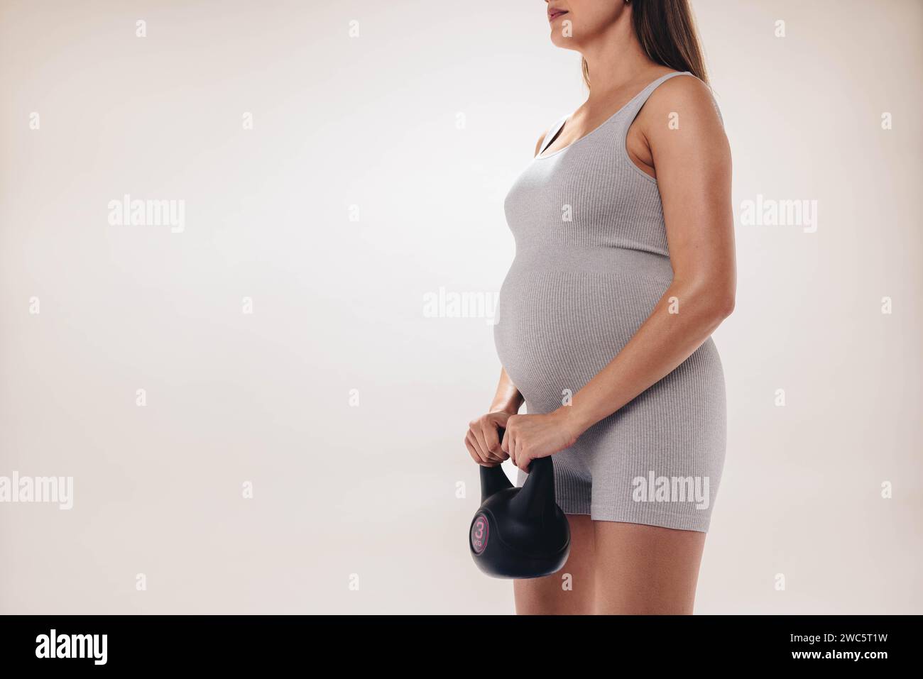 Donna con un batto del bambino che pratica l'allenamento della forza e il sollevamento pesi per un corpo sano durante la gravidanza. Indossa un abbigliamento fitness, tiene un manubrio Foto Stock