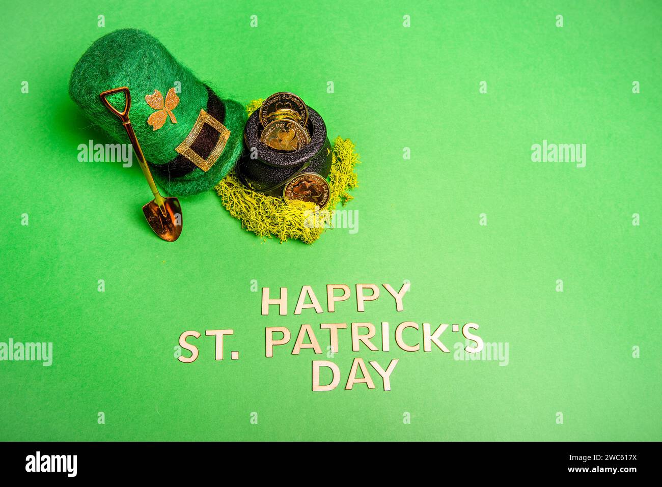 Vista dall'alto su uno sfondo verde e isolato si trovano l'iscrizione Happy Patrick's Day, Hat, leprechaun pot con monete d'oro, horseshoe per buona fortuna, pala Foto Stock