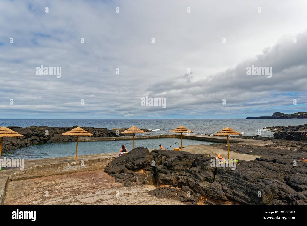 Piscina naturale sul mare con ombrelloni e persone rilassanti, passeggiata costiera sulle rocce laviche Ponta da Iiha, Calhau, costa occidentale, Pico, Azzorre Foto Stock