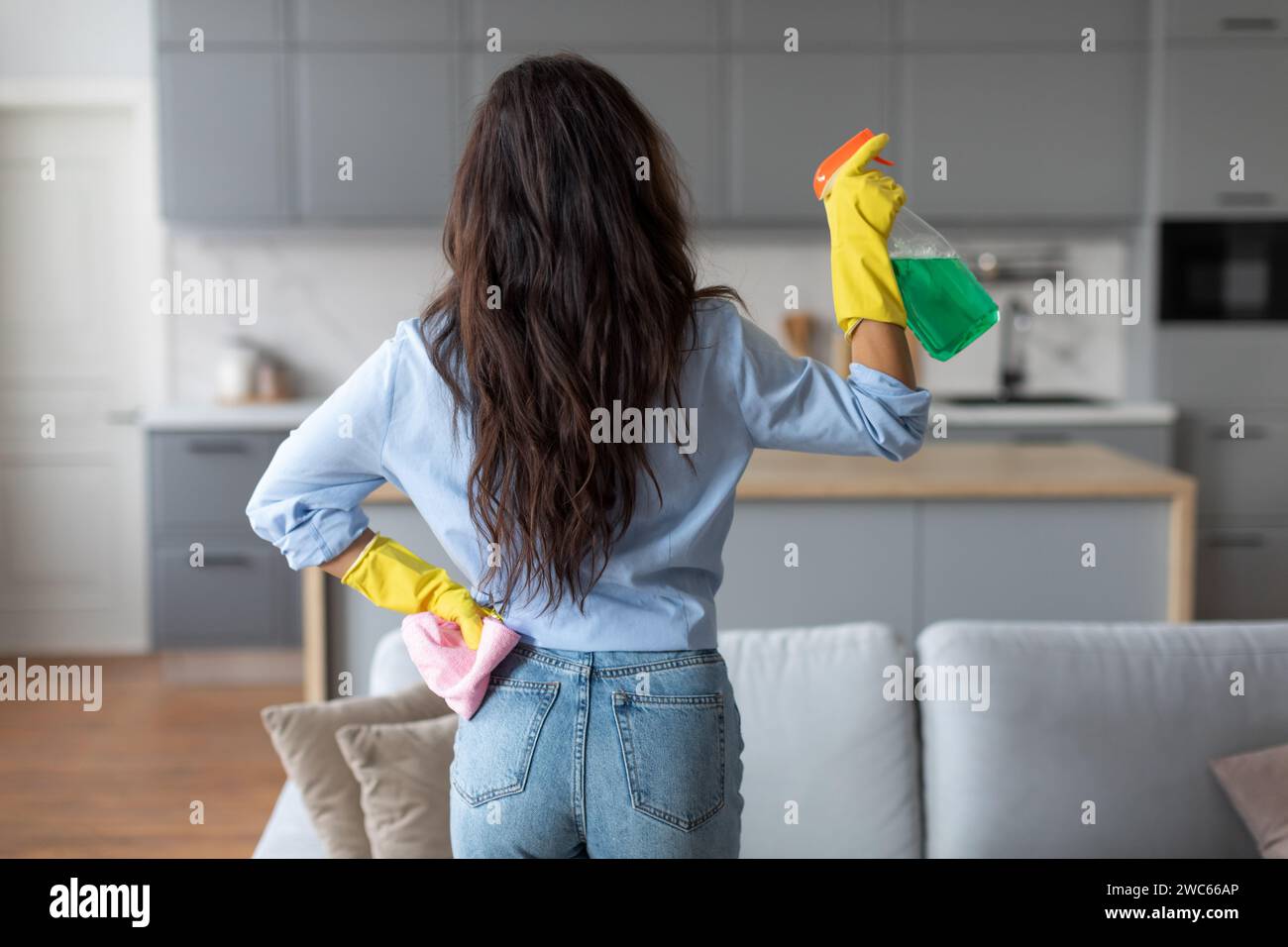 Donna in abbigliamento casual e guanti che pulisce con flacone spray Foto Stock