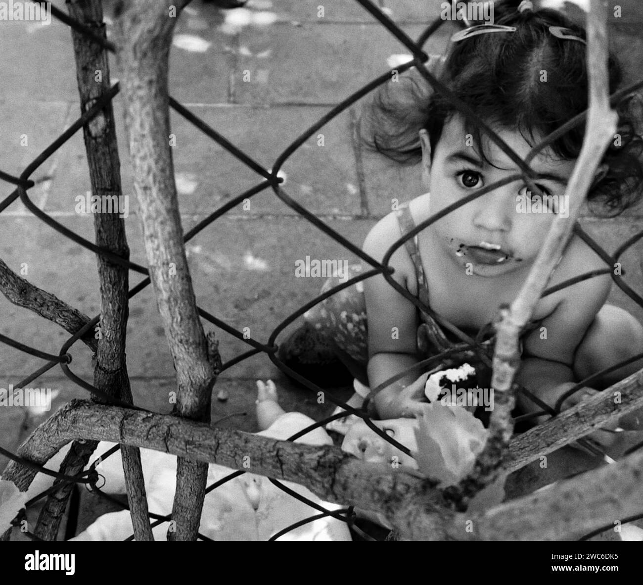 Un bambino che guarda curiosamente su una recinzione con un piatto di cibo per terra davanti a loro. Foto Stock