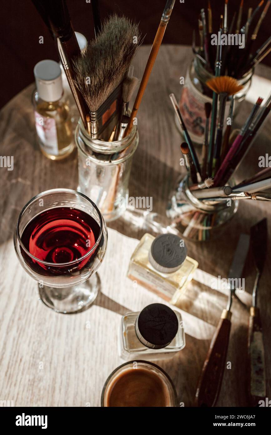 Vista dall'alto di un tavolo con strumenti di pittura, pennelli, olio, colori e bicchiere di vino rosso Foto Stock