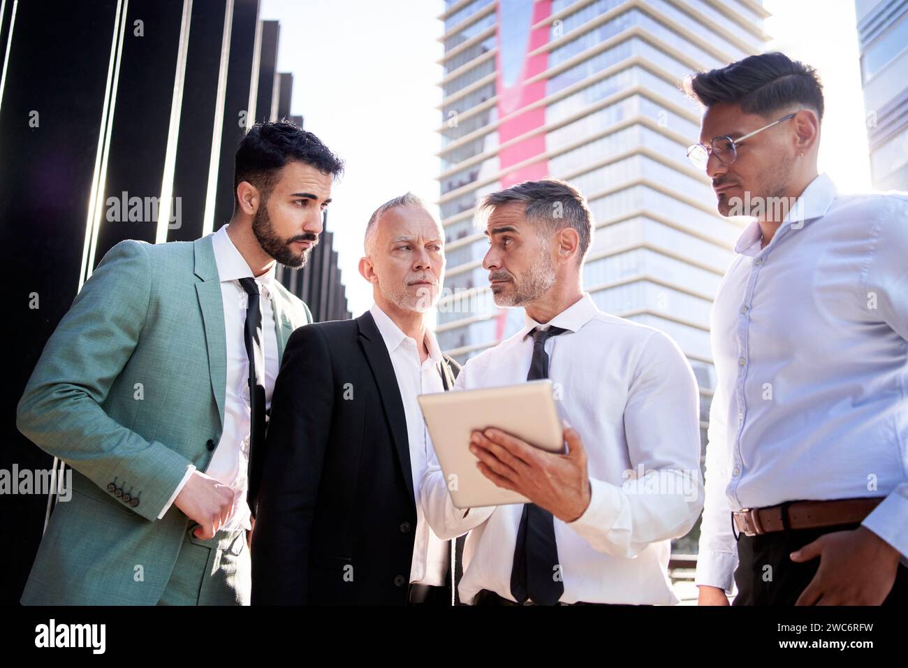 Gruppi di uomini d'affari si sono riuniti fuori da uffici che si guardano a vicenda consulenze seri su tablet. Foto Stock