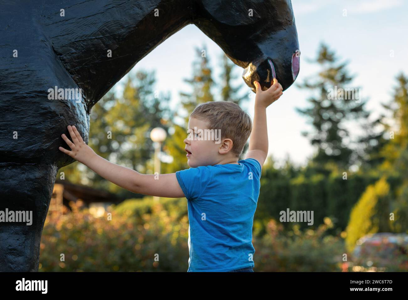 Ritratto ravvicinato di un bambino carino accanto al muso di un grosso cavallo di legno nero. Foto Stock