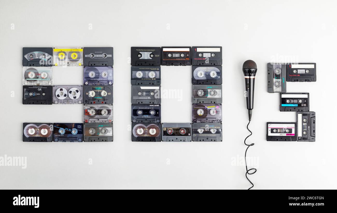Il testo "90's" su sfondo di carta grigia, composto da antiche, diverse e colorate cassette audio e microfono. L'anno della nostalgia per il karaoke partie Foto Stock