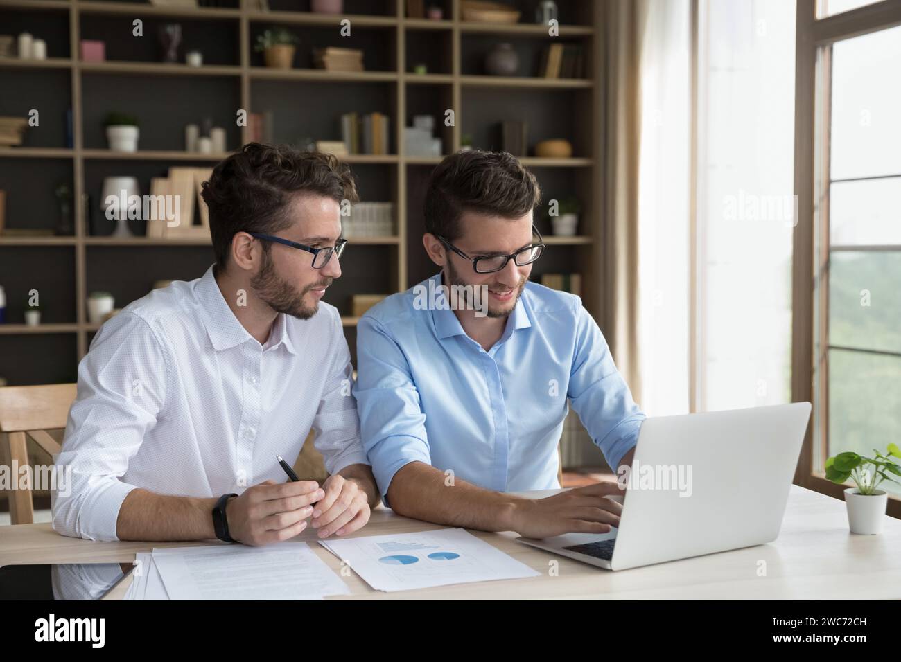 Due partner commerciali gemelli maschi siedono alla scrivania con un computer portatile Foto Stock